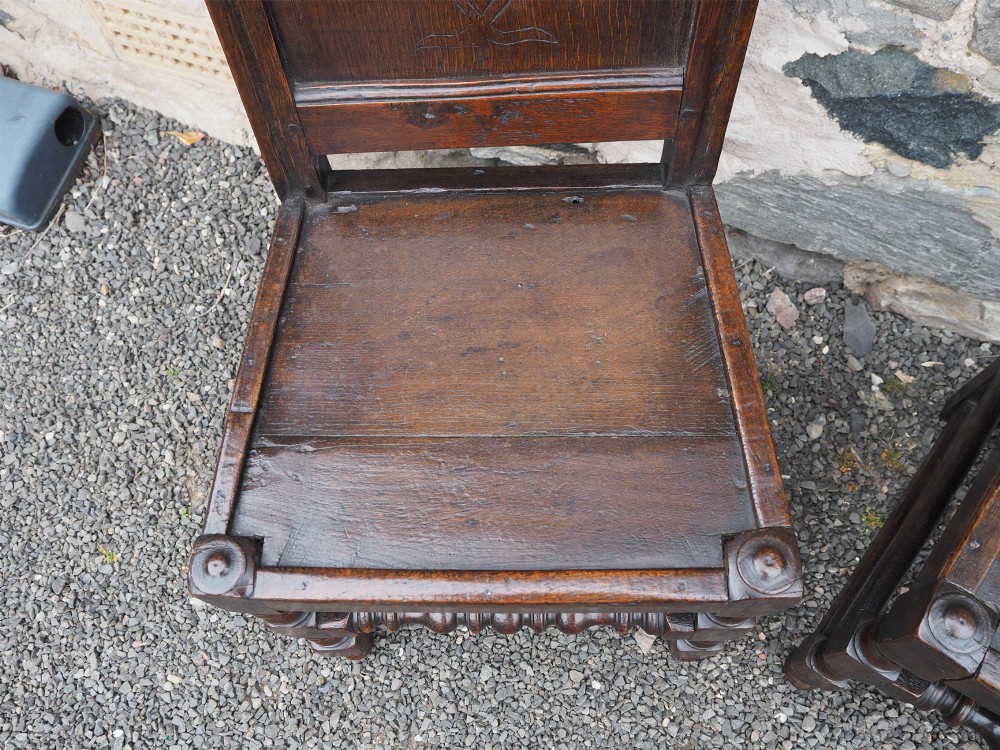 A pair of dark carved oak 17th-century hall chairs featuring geometric diamond back panels and turned legs. View VI