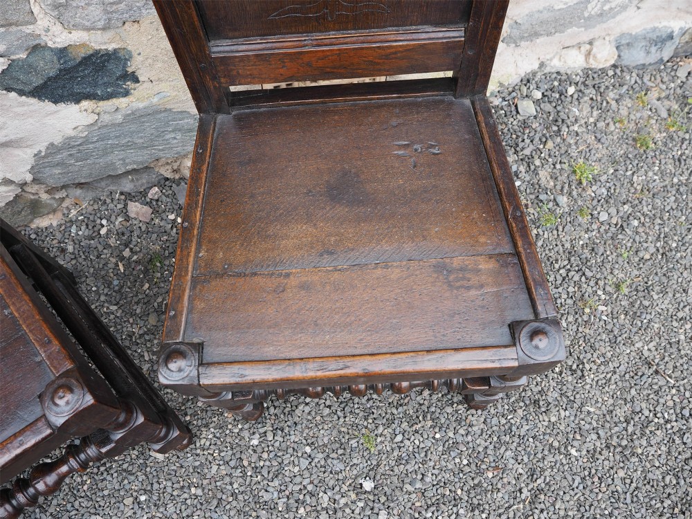 A pair of dark carved oak 17th-century hall chairs featuring geometric diamond back panels and turned legs. View VII