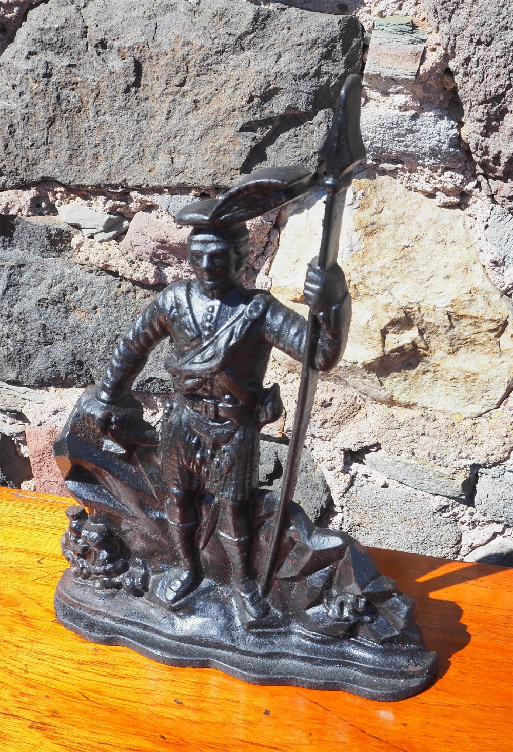 A black cast iron doorstop shaped as a Scottish Highlander warrior standing on a rocky base and holding a spear.