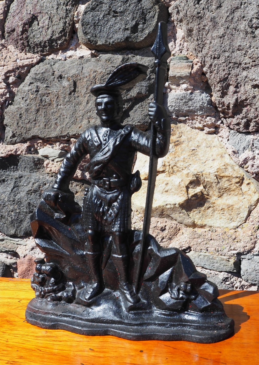 A black cast iron doorstop shaped as a Scottish Highlander warrior standing on a rocky base and holding a spear. View II