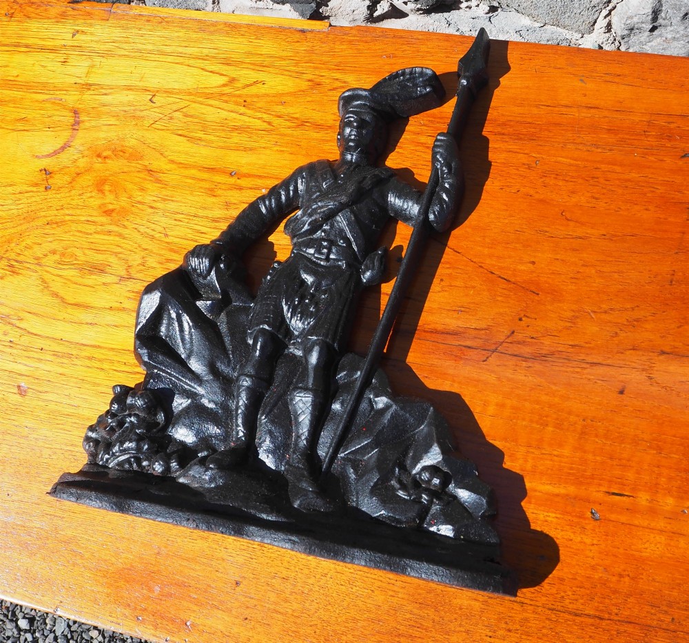 A black cast iron doorstop shaped as a Scottish Highlander warrior standing on a rocky base and holding a spear. View III