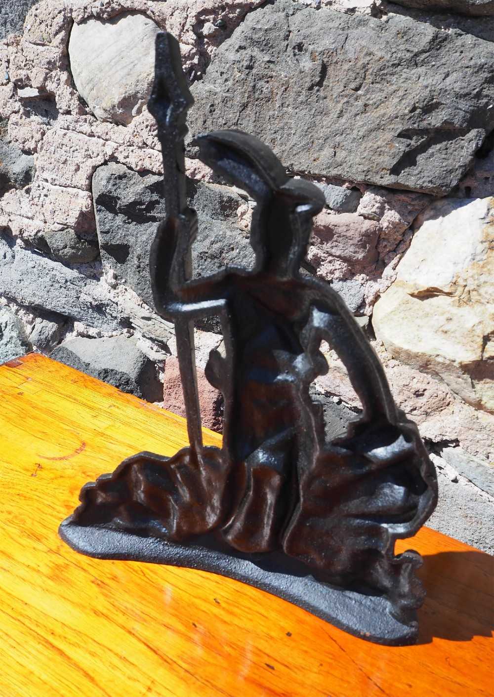 A black cast iron doorstop shaped as a Scottish Highlander warrior standing on a rocky base and holding a spear. View IV