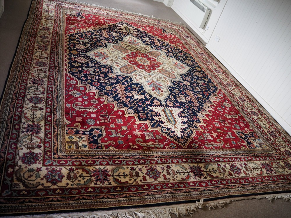 A large hand-knotted Persian wool carpet featuring a central cream medallion surrounded by navy blue and crimson sections filled with intricate floral motifs and framed by a detailed border.
