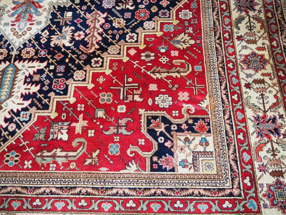 A large hand-knotted Persian wool carpet featuring a central cream medallion surrounded by navy blue and crimson sections filled with intricate floral motifs and framed by a detailed border. View IV