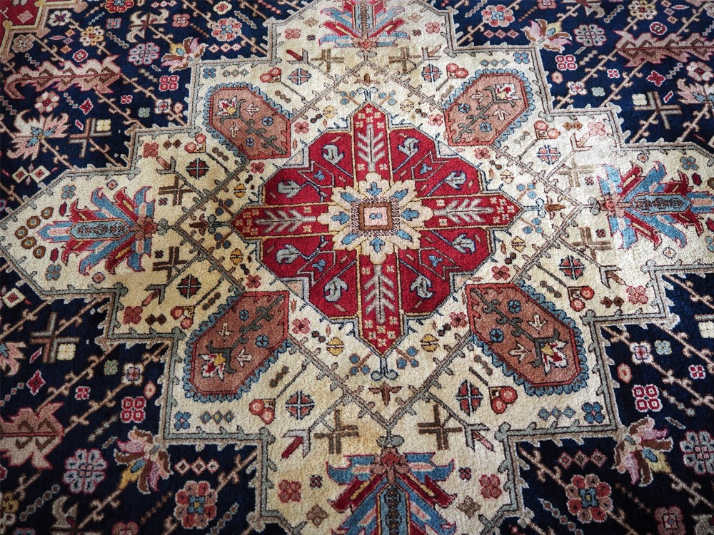 A large hand-knotted Persian wool carpet featuring a central cream medallion surrounded by navy blue and crimson sections filled with intricate floral motifs and framed by a detailed border. View VI