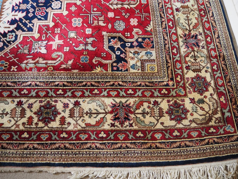 A large hand-knotted Persian wool carpet featuring a central cream medallion surrounded by navy blue and crimson sections filled with intricate floral motifs and framed by a detailed border. View VII