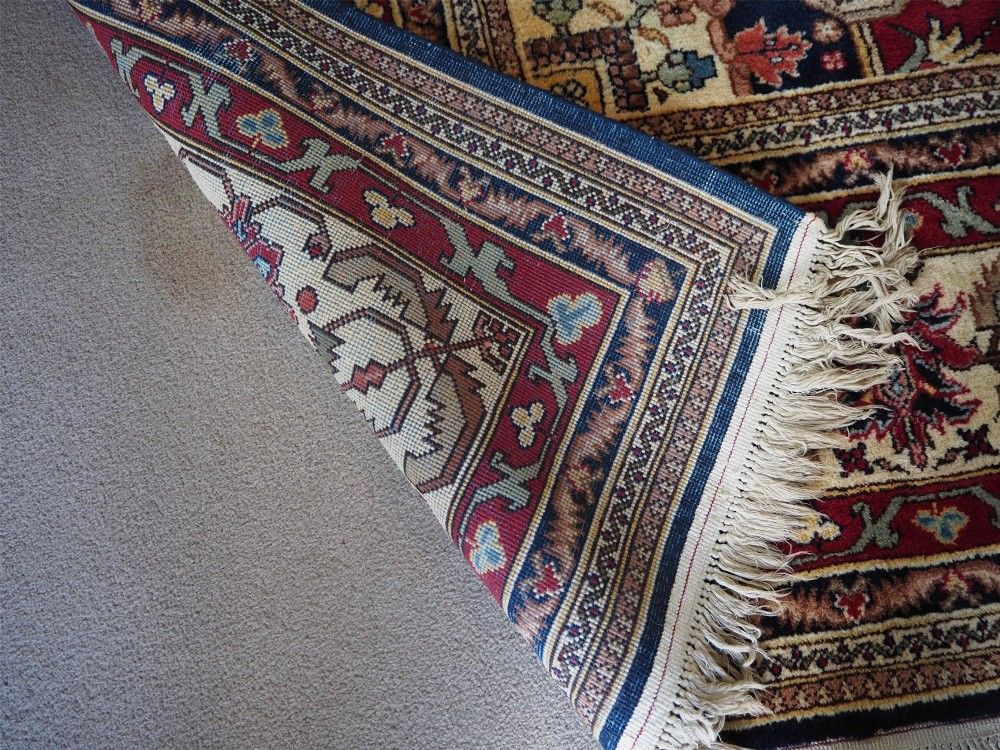 A large hand-knotted Persian wool carpet featuring a central cream medallion surrounded by navy blue and crimson sections filled with intricate floral motifs and framed by a detailed border. View X