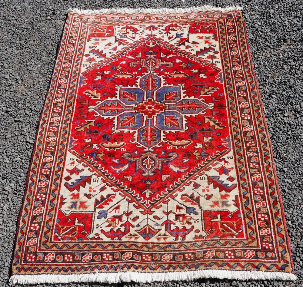 A small hand-knotted antique wool rug featuring a red central field with a blue star medallion, geometric cream spandrels, and a patterned border.