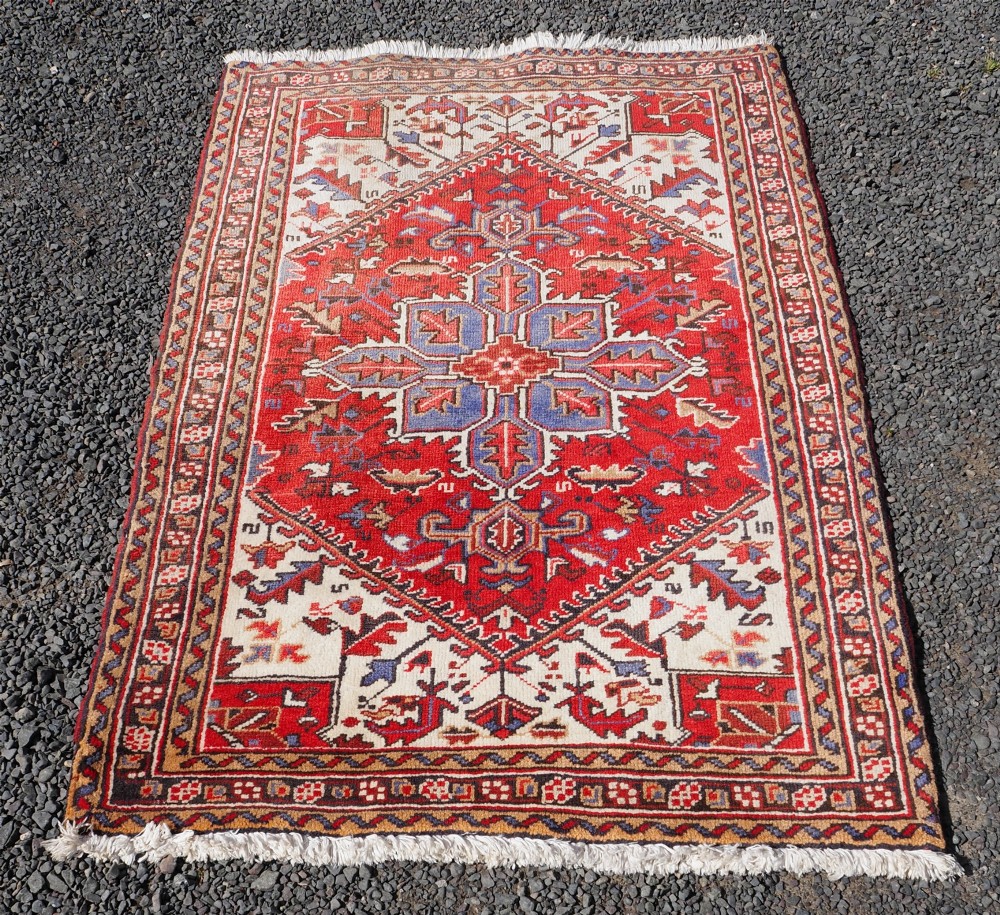 A small hand-knotted antique wool rug featuring a red central field with a blue star medallion, geometric cream spandrels, and a patterned border. View II