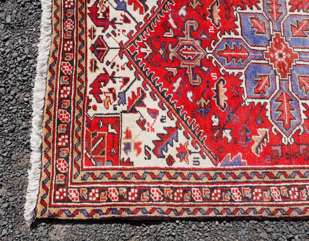 A small hand-knotted antique wool rug featuring a red central field with a blue star medallion, geometric cream spandrels, and a patterned border. View IV