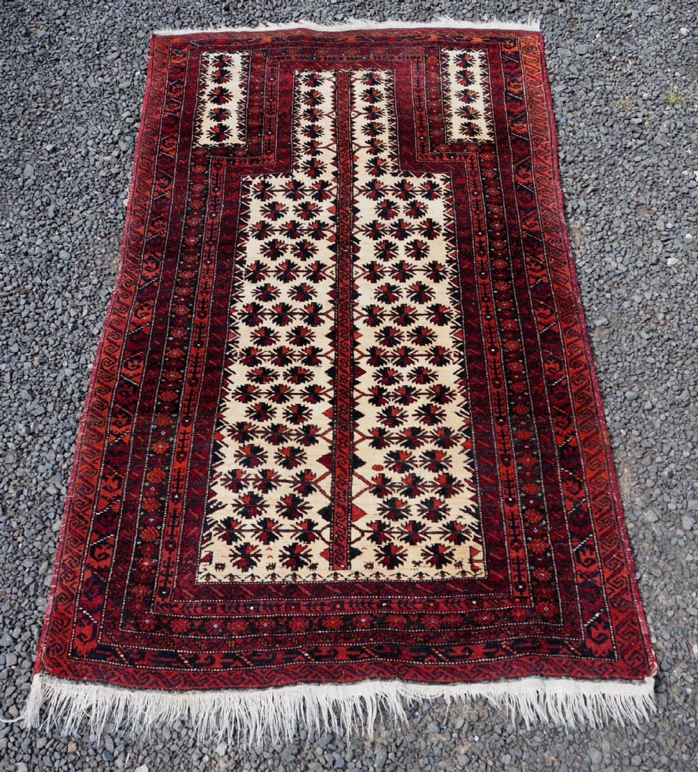 An antique hand-knotted Baluchi prayer rug featuring an off-white central field with geometric tree motifs framed by a deep red border.