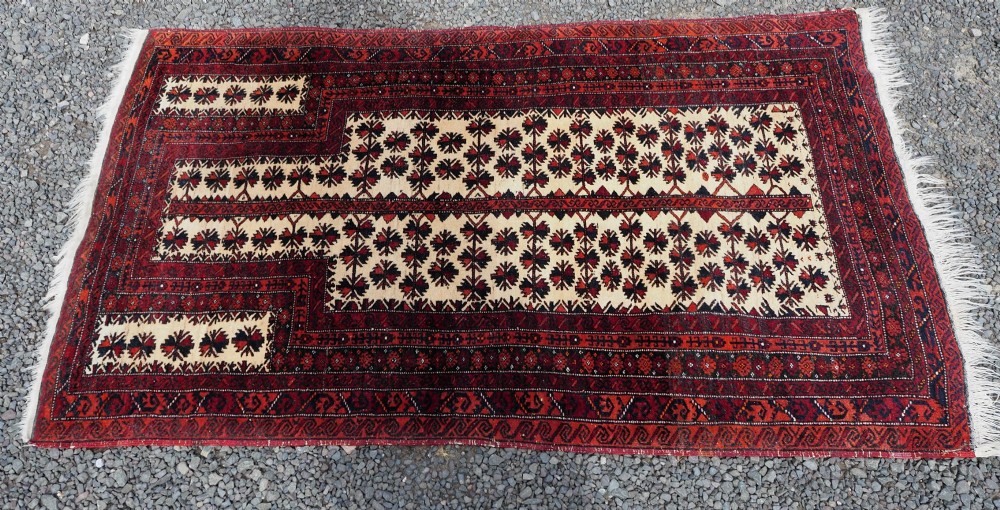 An antique hand-knotted Baluchi prayer rug featuring an off-white central field with geometric tree motifs framed by a deep red border. View III