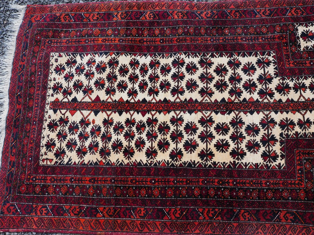 An antique hand-knotted Baluchi prayer rug featuring an off-white central field with geometric tree motifs framed by a deep red border. View V