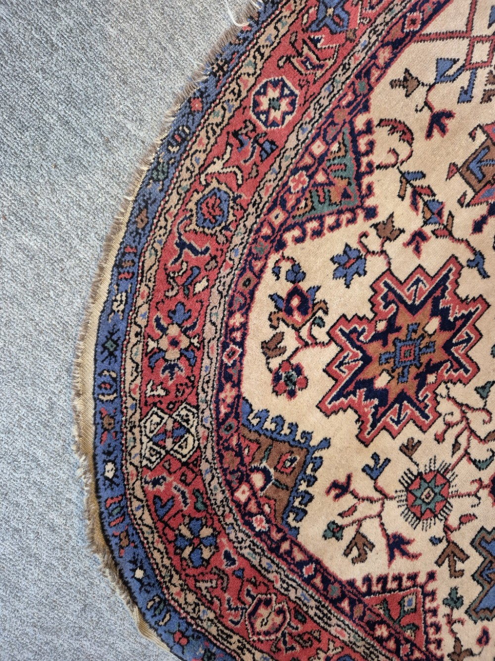 An antique hand-knotted Persian Bijar rug featuring a central terracotta medallion, geometric blue and red star motifs, a cream ground, and rounded curved ends. View VI