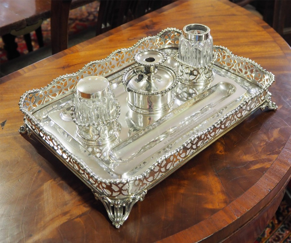 An antique silver-plated rectangular desk tray featuring a pierced gallery edge, two cut glass inkwells, a central taper holder, and a recessed pen groove. View II