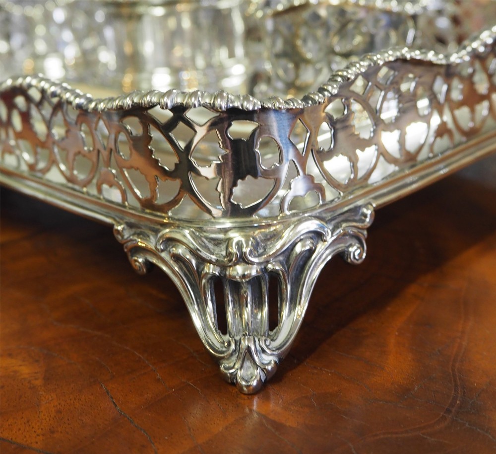 An antique silver-plated rectangular desk tray featuring a pierced gallery edge, two cut glass inkwells, a central taper holder, and a recessed pen groove. View V