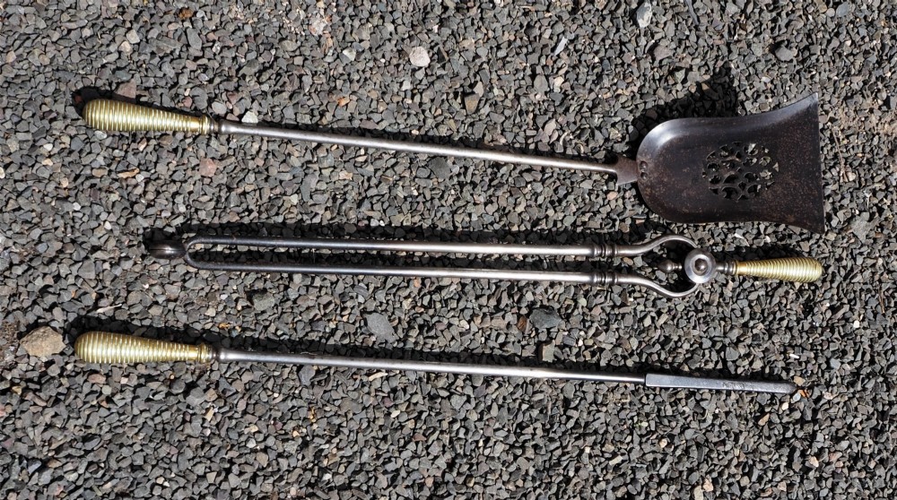 A three-piece set of 18th-century steel fire irons featuring turned brass beehive handles and a pierced shovel pan. View II
