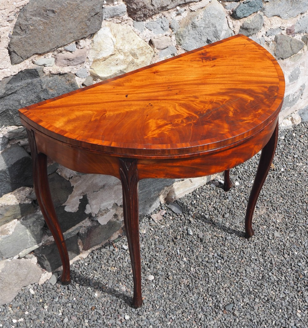 An 18th-century demilune folding card table crafted with flame mahogany veneer and carved slender legs. View II