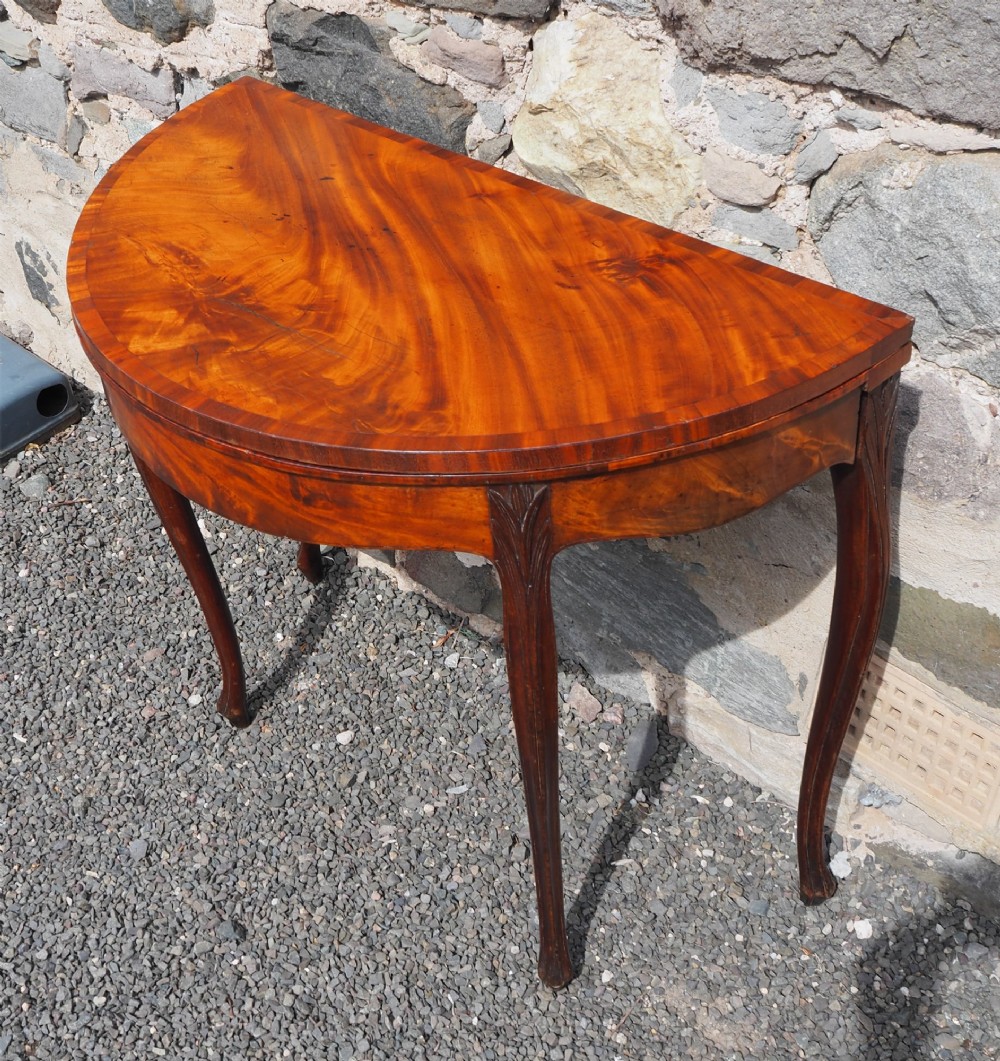 An 18th-century demilune folding card table crafted with flame mahogany veneer and carved slender legs. View III