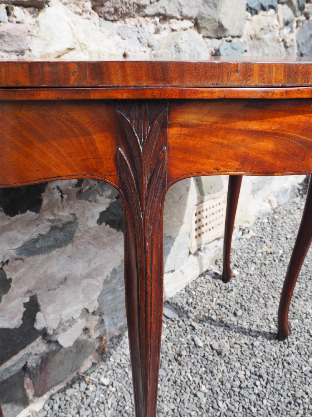 An 18th-century demilune folding card table crafted with flame mahogany veneer and carved slender legs. View V