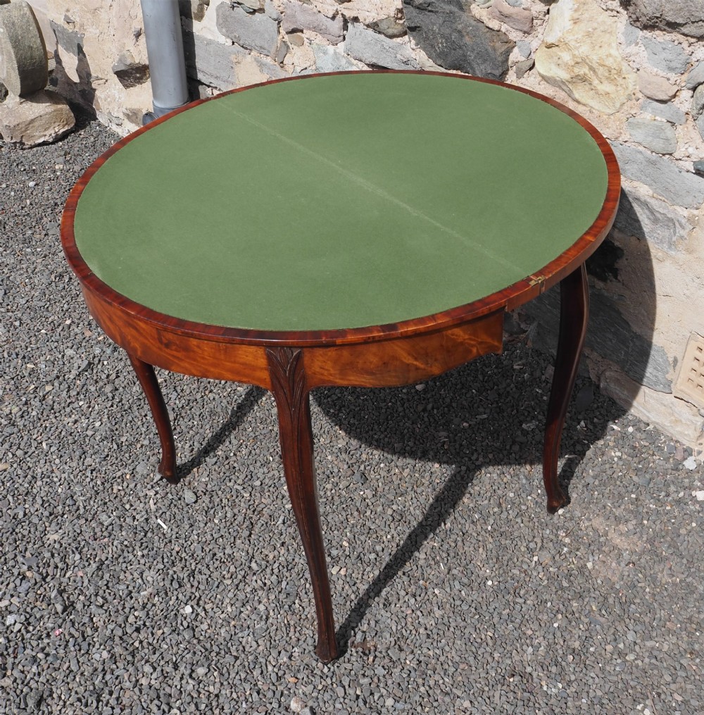 An 18th-century demilune folding card table crafted with flame mahogany veneer and carved slender legs. View VII