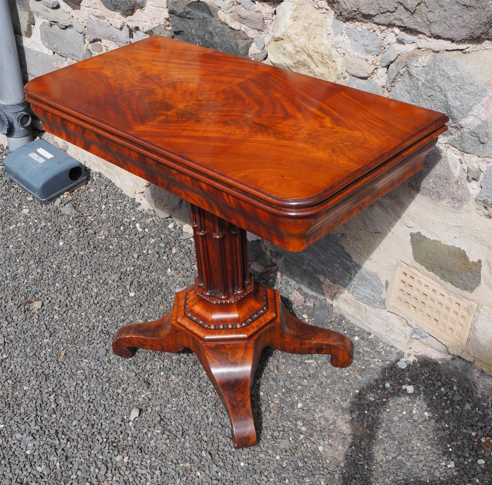An 1830s William IV flame mahogany tea table featuring a fold-over rectangular top set on a fluted pedestal column with a four-point platform base and scroll feet. View II