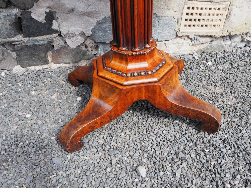 An 1830s William IV flame mahogany tea table featuring a fold-over rectangular top set on a fluted pedestal column with a four-point platform base and scroll feet. View IV