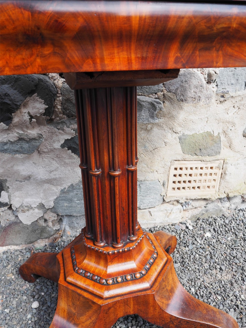 An 1830s William IV flame mahogany tea table featuring a fold-over rectangular top set on a fluted pedestal column with a four-point platform base and scroll feet. View V