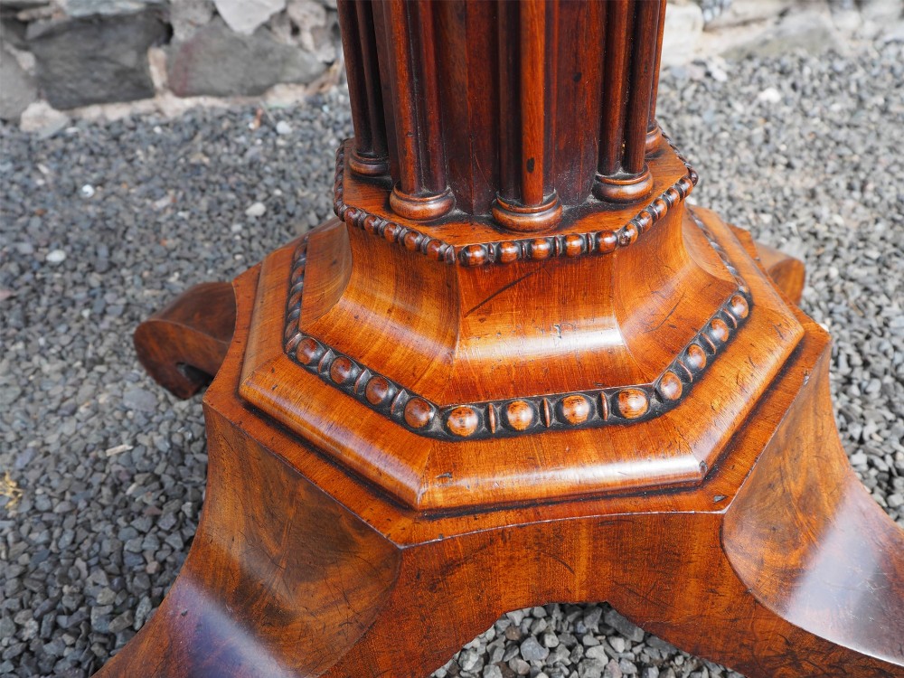 An 1830s William IV flame mahogany tea table featuring a fold-over rectangular top set on a fluted pedestal column with a four-point platform base and scroll feet. View VI