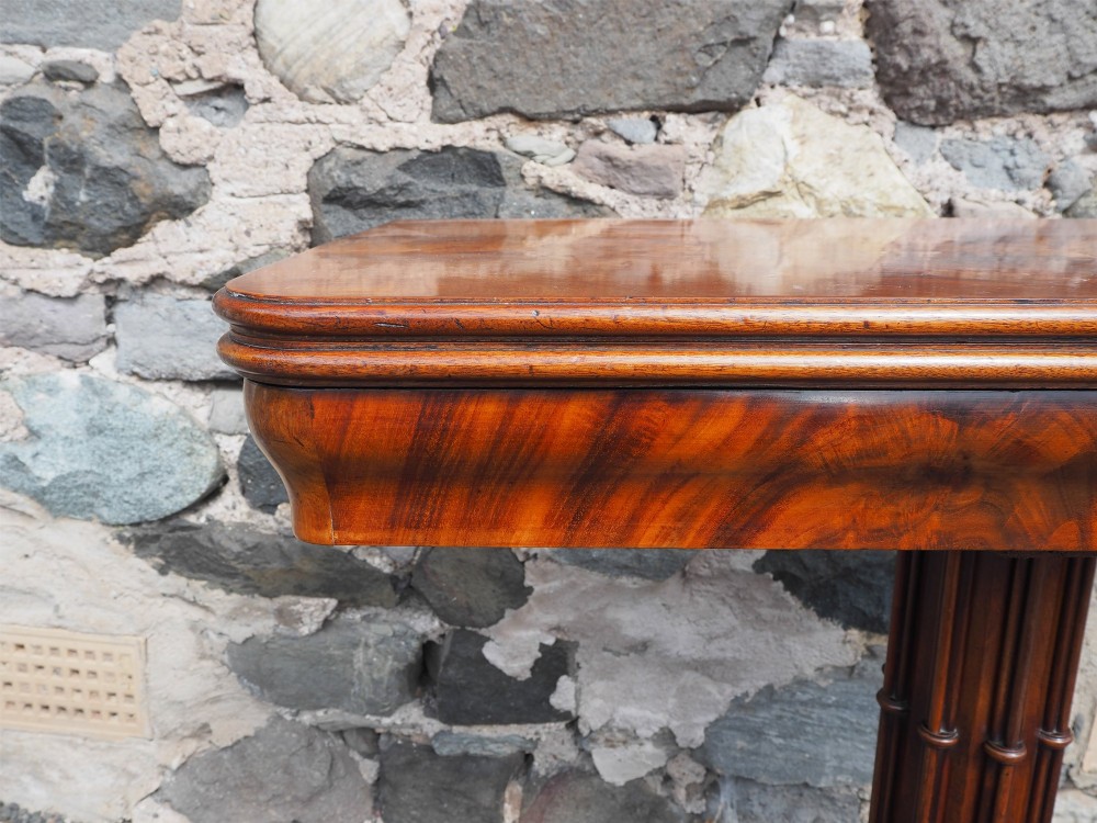 An 1830s William IV flame mahogany tea table featuring a fold-over rectangular top set on a fluted pedestal column with a four-point platform base and scroll feet. View VII