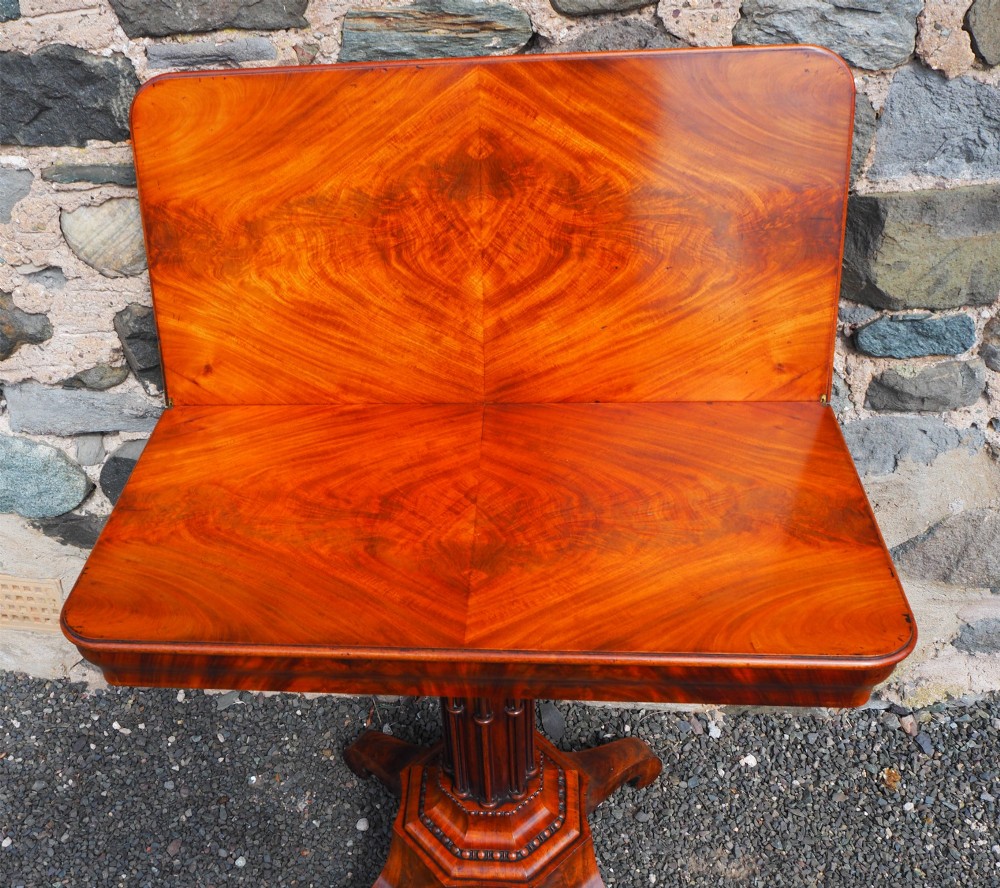An 1830s William IV flame mahogany tea table featuring a fold-over rectangular top set on a fluted pedestal column with a four-point platform base and scroll feet. View VIII
