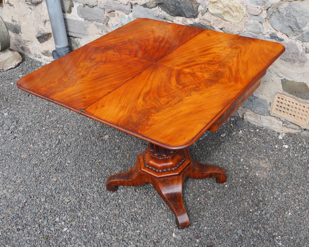 An 1830s William IV flame mahogany tea table featuring a fold-over rectangular top set on a fluted pedestal column with a four-point platform base and scroll feet. View IX