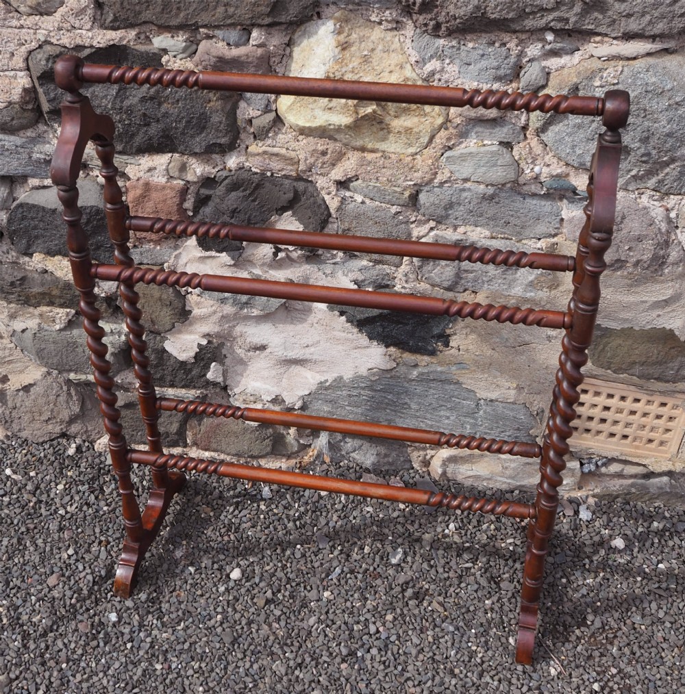 A freestanding Edwardian mahogany towel rail featuring barley twist turned uprights, horizontal crossbars, and curved trestle feet.