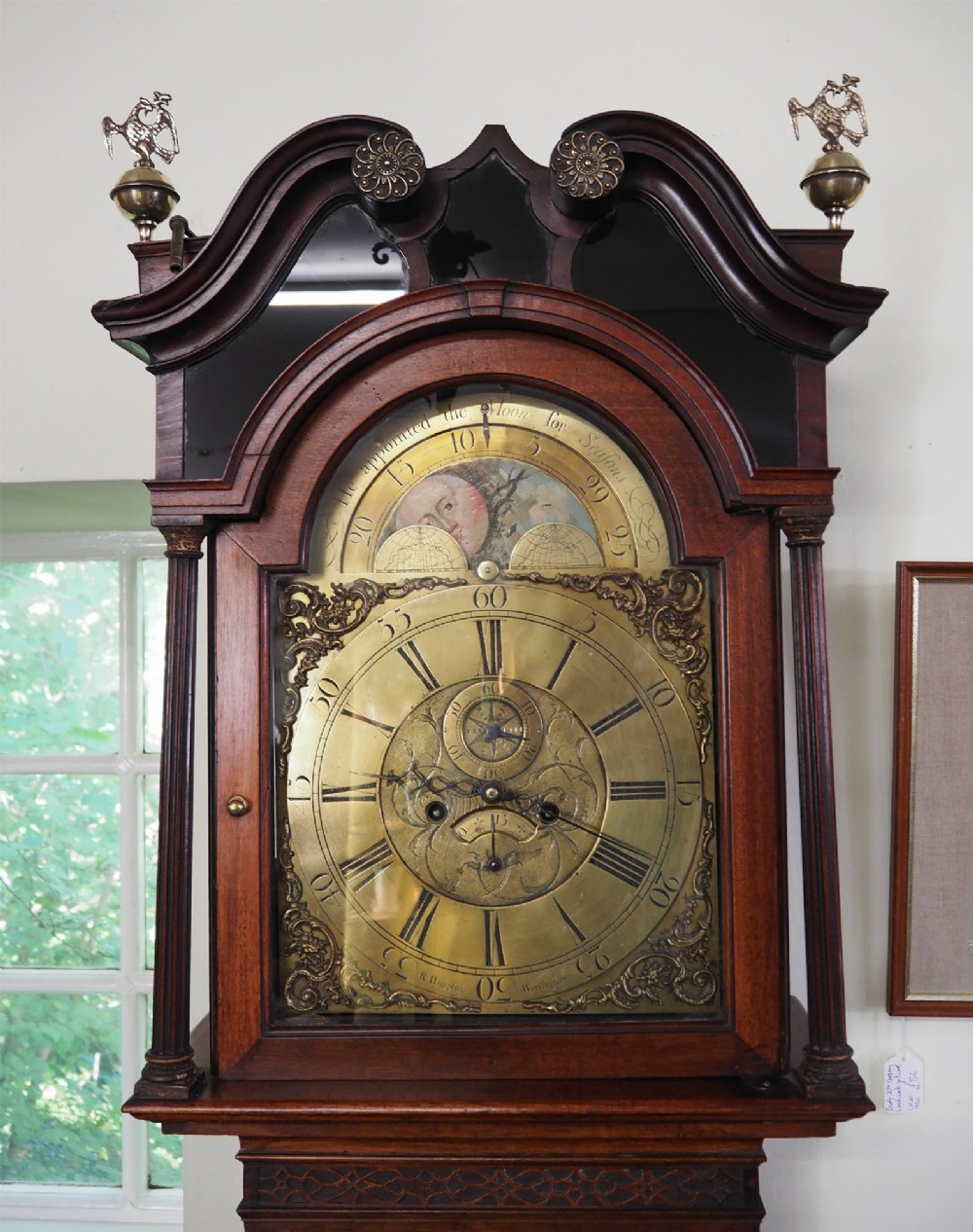 An eighteenth-century mahogany longcase clock featuring a swan-neck pediment with brass finials, an ornate brass dial with a moon phase arch, and a flame mahogany veneer trunk door. View II