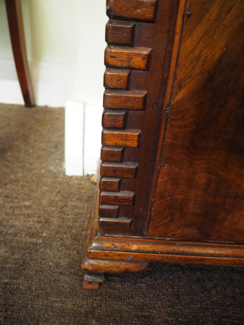 An eighteenth-century mahogany longcase clock featuring a swan-neck pediment with brass finials, an ornate brass dial with a moon phase arch, and a flame mahogany veneer trunk door. View V