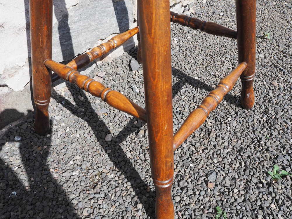A 19th-century high stool constructed from ash and beech timber, featuring turned splayed legs, foot stretchers, and a rounded wooden seat. View V