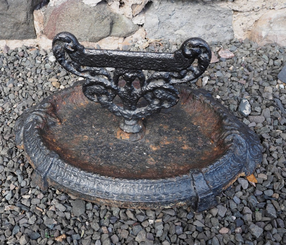 A Victorian cast iron boot scraper featuring a scrollwork top blade mounted above an oval tray with a textured border.