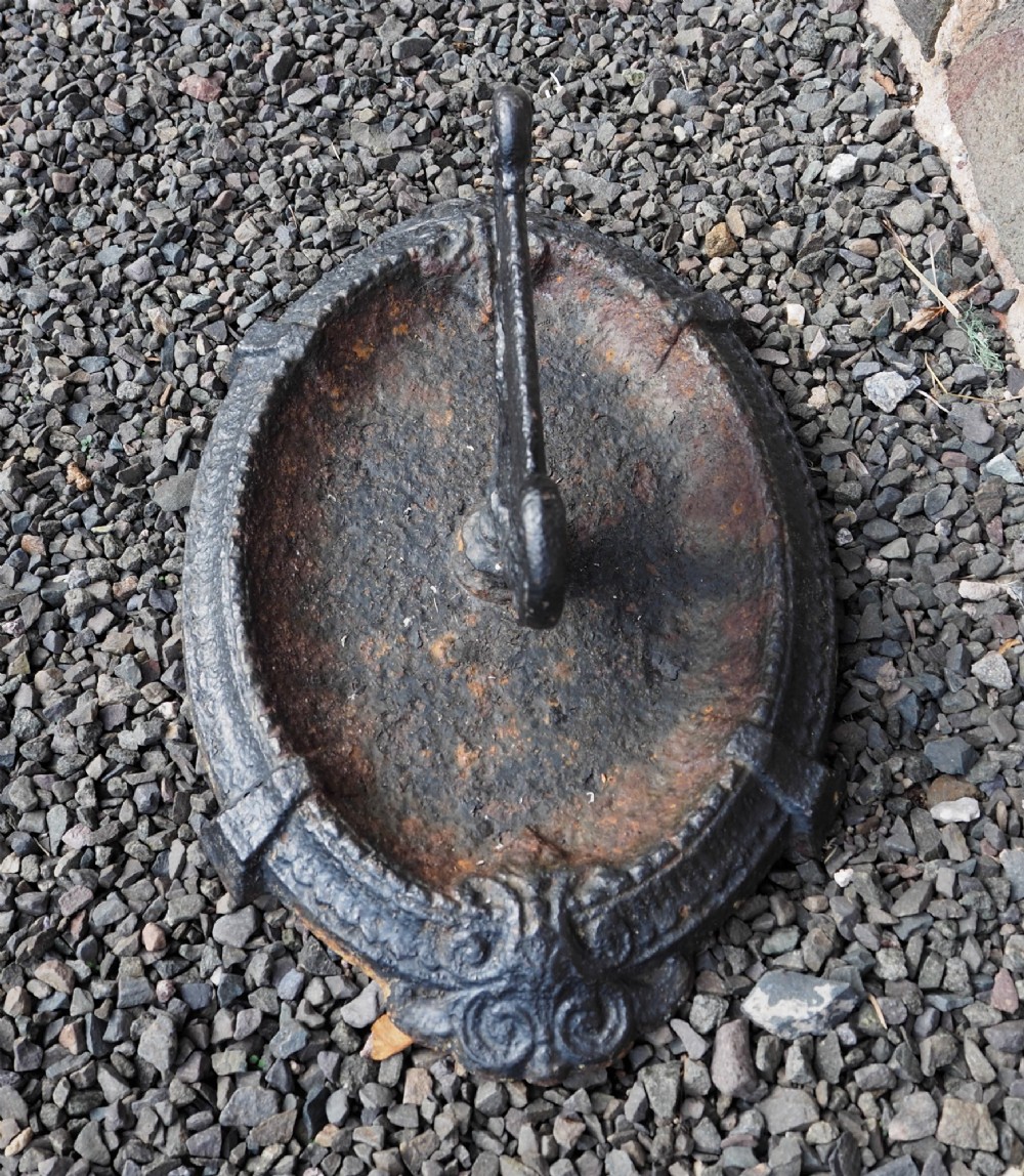 A Victorian cast iron boot scraper featuring a scrollwork top blade mounted above an oval tray with a textured border. View III