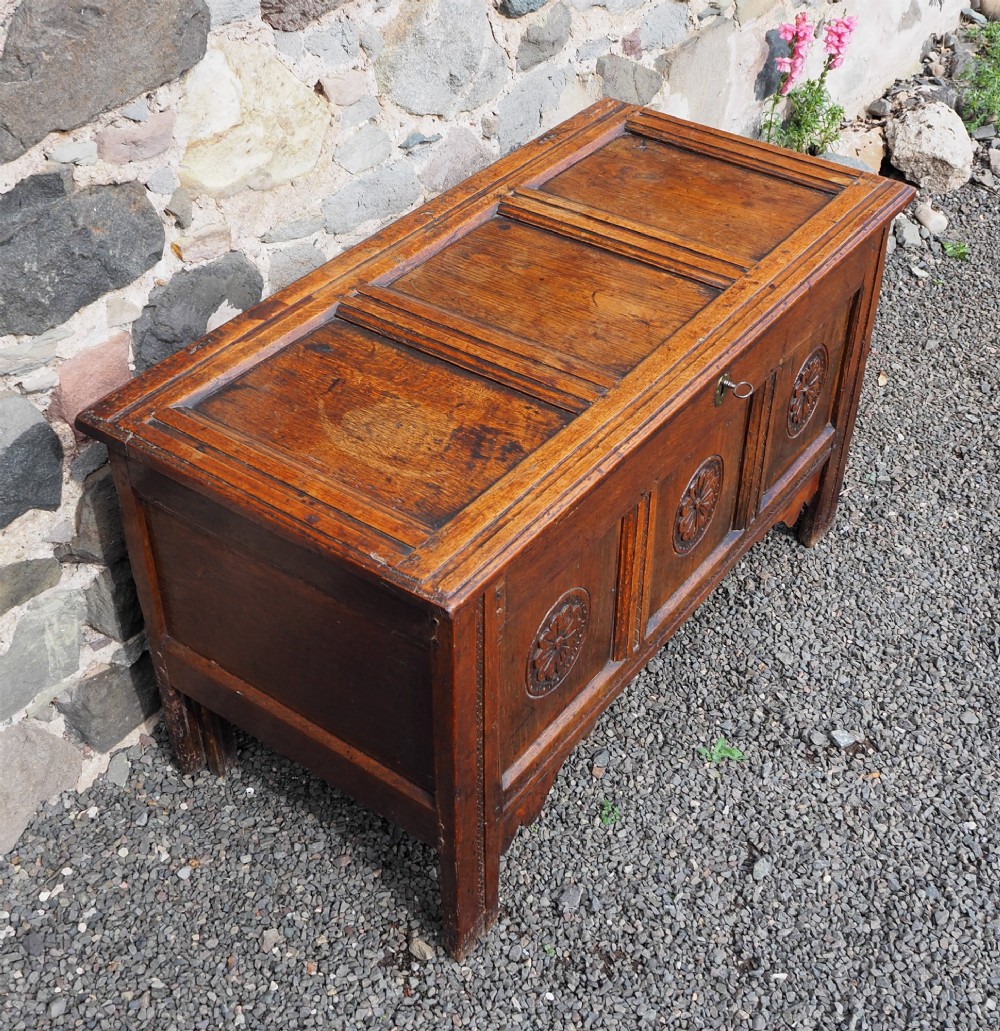 An early 18th-century oak coffer with a three-panel hinged top, carved rosette panels on the front, and a brass keyhole escutcheon. View III