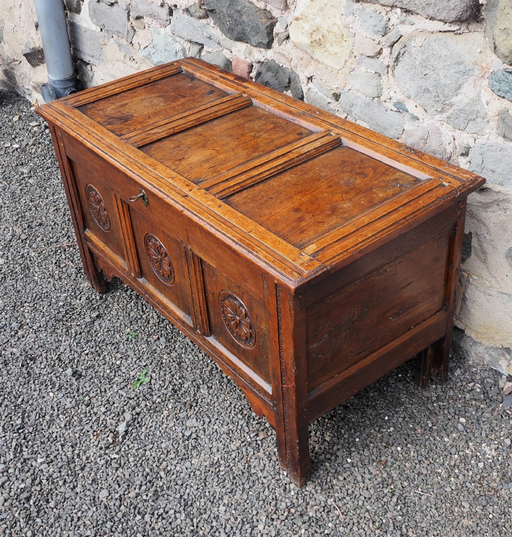 An early 18th-century oak coffer with a three-panel hinged top, carved rosette panels on the front, and a brass keyhole escutcheon. View IV