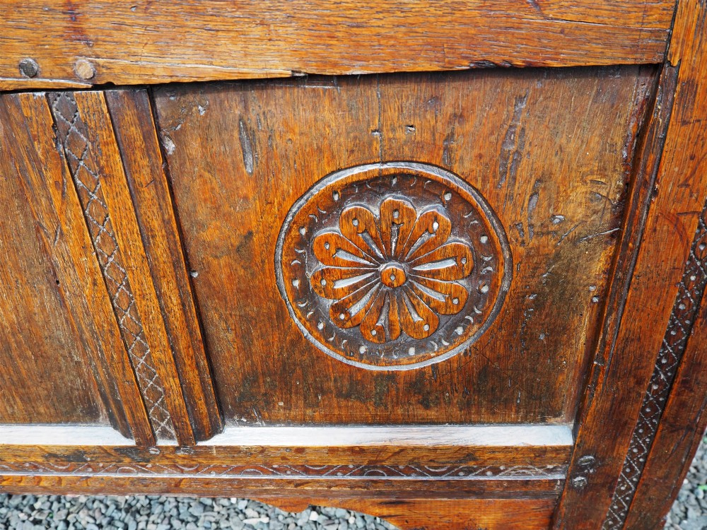 An early 18th-century oak coffer with a three-panel hinged top, carved rosette panels on the front, and a brass keyhole escutcheon. View VI
