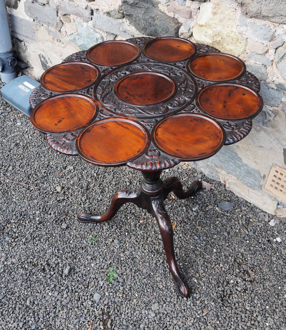 A Chippendale style dark mahogany tilt-top supper table featuring eight carved dished plate compartments around a central recess on a tripod cabriole base. View II