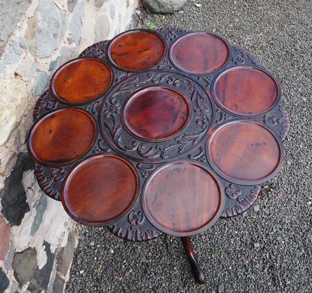 A Chippendale style dark mahogany tilt-top supper table featuring eight carved dished plate compartments around a central recess on a tripod cabriole base. View III