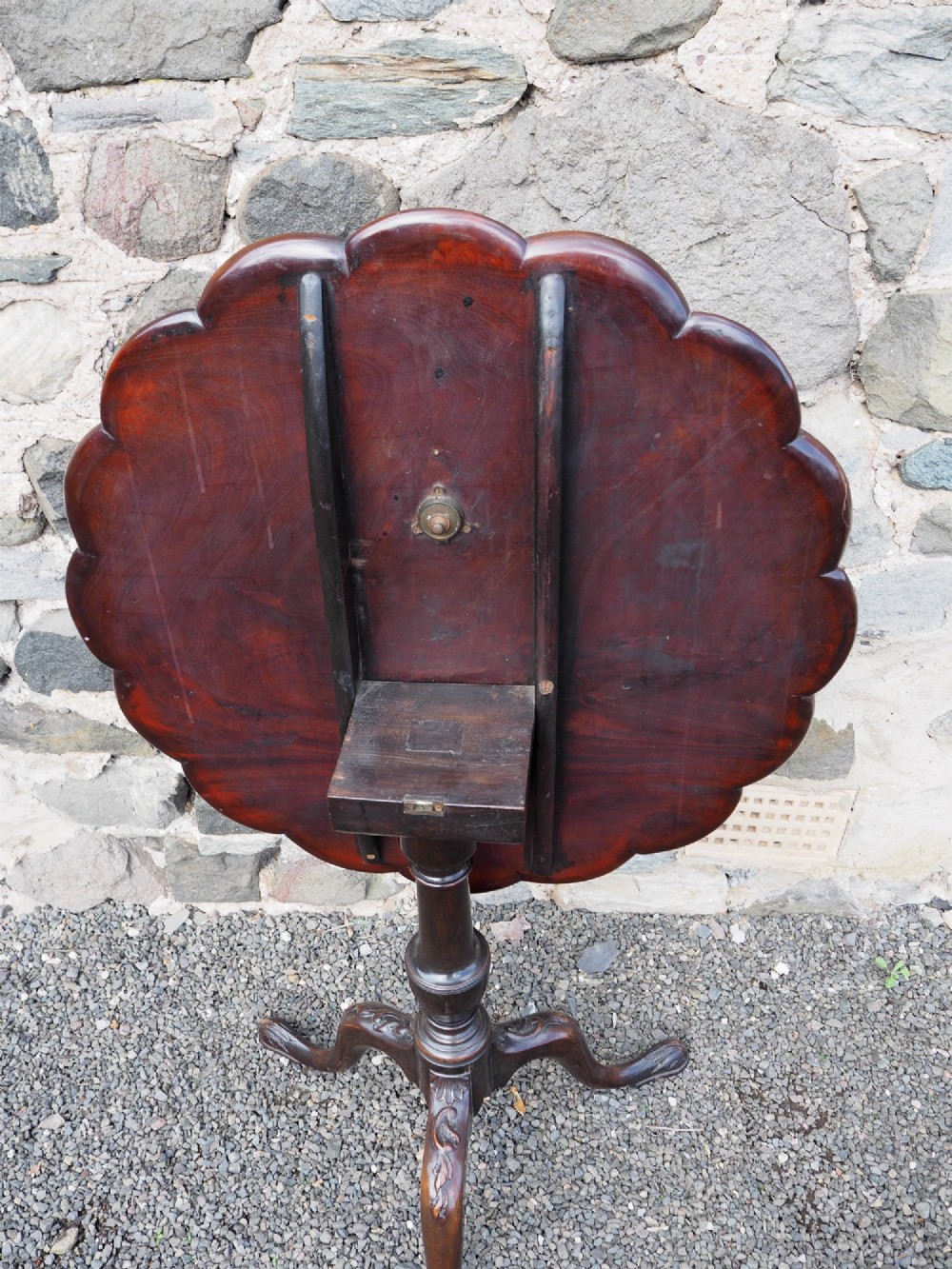 A Chippendale style dark mahogany tilt-top supper table featuring eight carved dished plate compartments around a central recess on a tripod cabriole base. View V