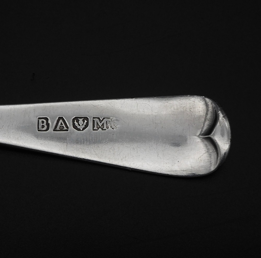 An antique silver sauce ladle with a deep circular bowl and a slender plain stem against a dark background. View V
