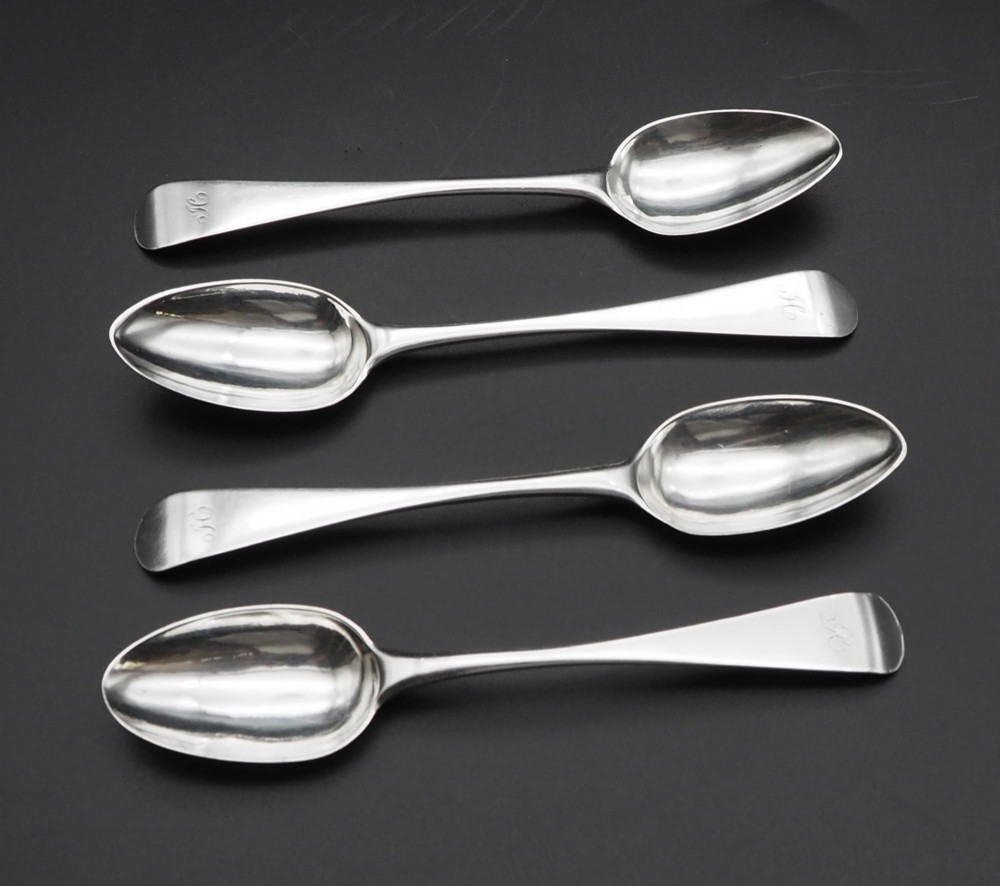 A set of four antique Scottish silver teaspoons with engraved terminal monograms displayed against a dark background.