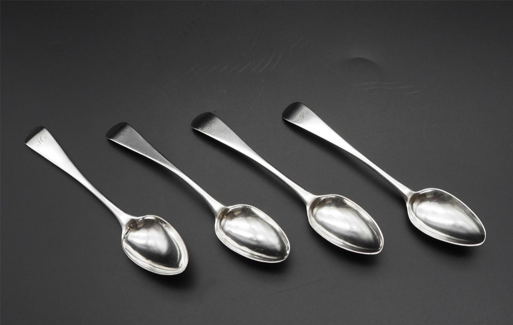 A set of four antique Scottish silver teaspoons with engraved terminal monograms displayed against a dark background. View II