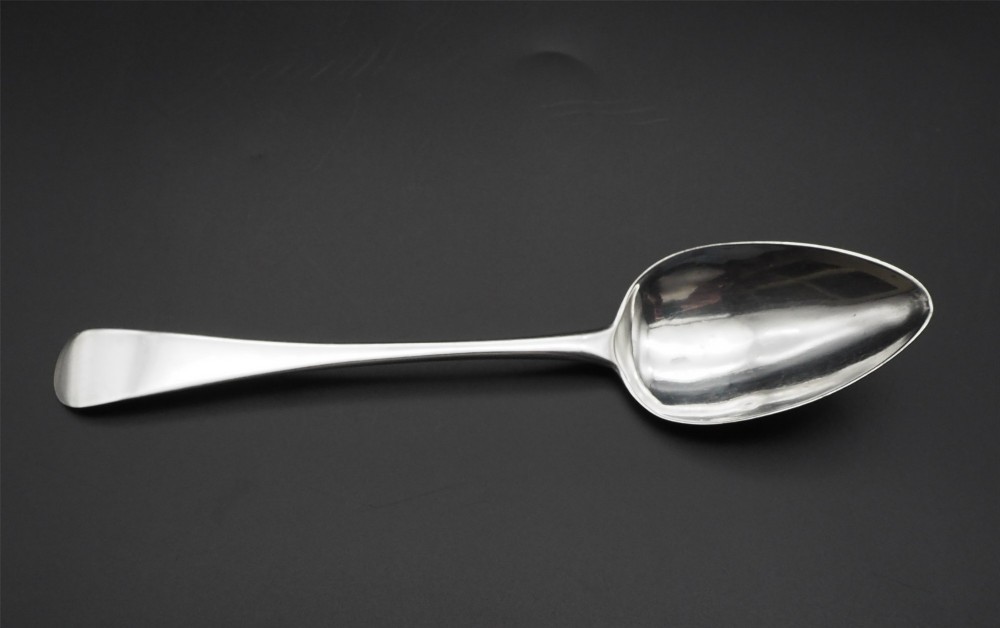 A set of four polished antique silver serving spoons with smooth handles and oval bowls arranged on a dark backdrop. View III