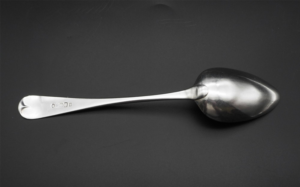 A set of four polished antique silver serving spoons with smooth handles and oval bowls arranged on a dark backdrop. View IV