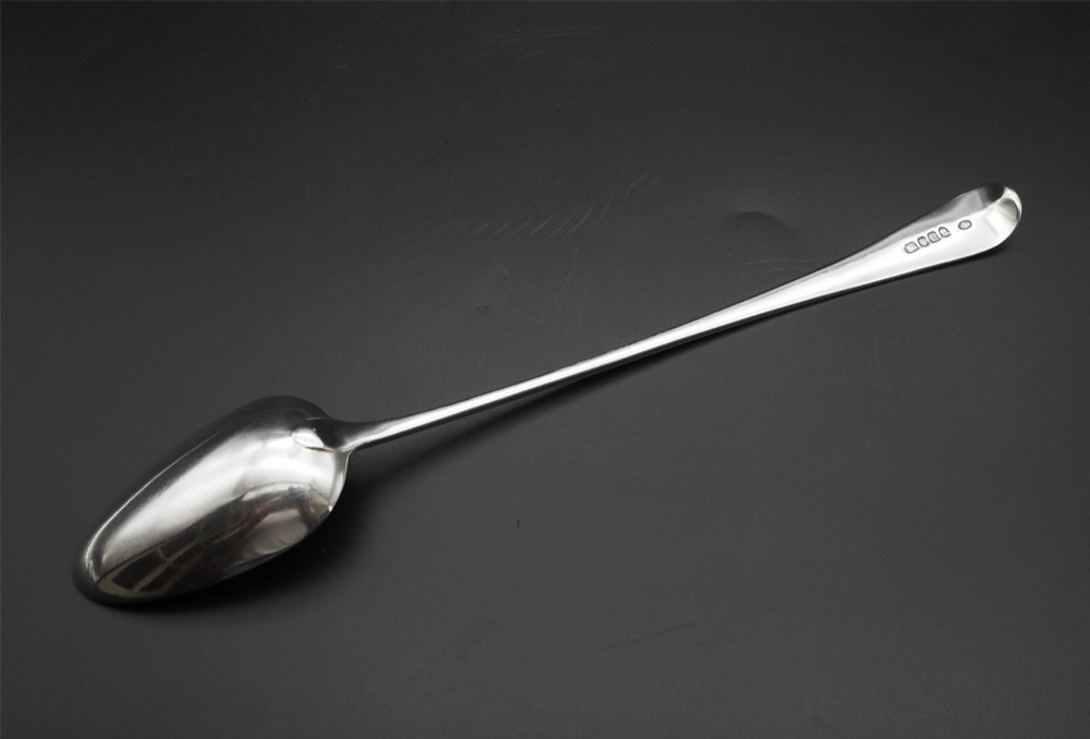A Georgian sterling silver basting spoon featuring an elongated stem and deep oval bowl on a dark surface. View III
